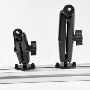 Pode incluir: Dois braços de articulação dupla pretos com botões de aperto, montados num trilho de extrusão de alumínio prateado. Cada braço possui uma placa superior circular com um parafuso metálico central para fixar equipamentos com segurança.