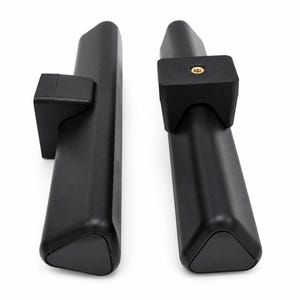 May include: Two black, triangular-shaped mounting bars with matte finishes. Each bar features a rectangular bracket attached to the side. One bracket displays a centred, circular brass-coloured threaded metal insert for secure attachment.