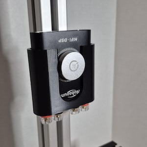 Op de afbeelding: Een zwart HiFi DSP audio component met een zilveren bedieningsknop. Het apparaat heeft de tekst "HiFi DSP" en de merknaam "Nobosoun". Het component is gemonteerd op een zilveren metalen frame en heeft rode en transparante connectoren.