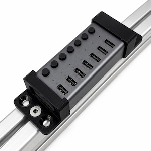 May include: A dark gray USB 3.0 hub with seven ports and seven individual black power buttons, mounted in a black 3D-printed bracket attached to a silver aluminum extrusion profile with a visible metal bolt and three circular mounting holes.