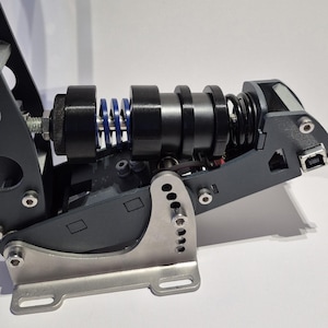 May include: Close-up of a racing simulator pedal assembly. The assembly features a combination of black, silver, and blue components, including springs, cylinders, and a mounting bracket. The design suggests a focus on precision and performance.