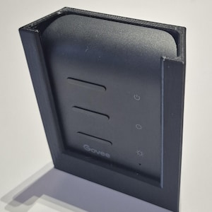 May include: A black Govee smart home device with a rectangular design. The device has three horizontal lines and three illuminated icons. The Govee logo is visible. The device is mounted in a black frame.