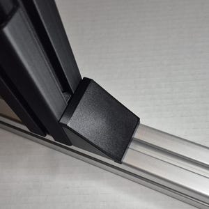 Puede incluir: Un soporte negro impreso en 3D con una base rectangular y un soporte en ángulo, montado sobre un riel de metal plateado. El soporte parece estar diseñado para soporte estructural o fines de montaje. La imagen está tomada en ángulo.