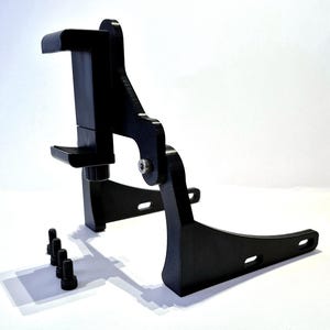 May include: A black adjustable phone mount stand featuring a vertical clamp mechanism with a tension knob, connected to a curved base with slotted mounting holes, accompanied by four separate black metal bolts for assembly and installation.