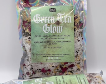 May include: A clear, iridescent bag filled with bath salts, dried florals, and essential oils. The bag features a green label with the text "Green Tea Glow" and product details. The net weight is 5.7 oz (170 g).