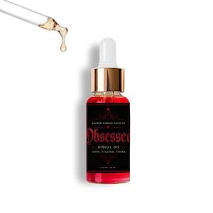 May include: A clear glass dropper bottle filled with red liquid, featuring a black label with red text reading Sacred Baddie Society, Obsessed Ritual Oil, Love. Fixated. Yours. 1 fl oz / 30 ml. A separate glass dropper tip is shown above with a golden drop.