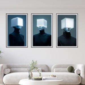 May include: Three framed art prints featuring figures with glowing white cube-shaped headpieces. The figures wear black turtlenecks against a blue-toned background. The artwork is displayed above a modern, curved sofa.