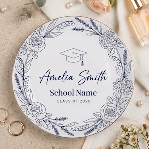 Op de afbeelding: Een witte keramische mok met een zwarte handgreep en de tekst "But First, Coffee" in een vetgedrukte, zwarte letter. De mok staat tegen een wazige achtergrond, wat een gezellige setting suggereert.