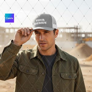 May include: A gray trucker hat with the text "YOUR DESIGN" in white. The hat has a white mesh back and a gray front panel. The person in the image is wearing an olive green jacket.