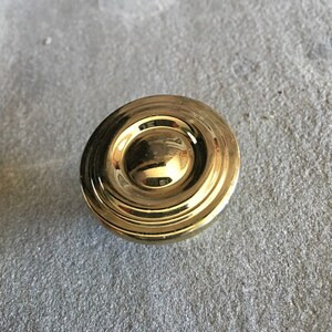 May include: A gold-toned round cabinet knob with a raised, concentric circle design.