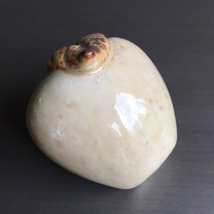 May include: A white ceramic vase with a brown and white swirl design on the top. The vase is shaped like a pear.