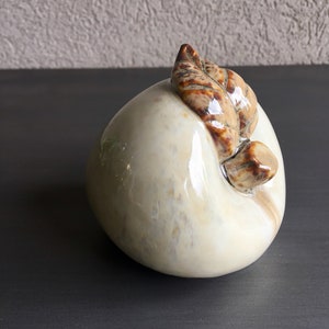 May include: A white ceramic peach figurine with a brown leaf detail. The peach has a glossy finish and a slightly textured surface.