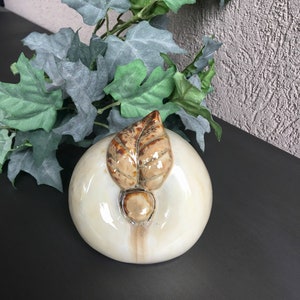 May include: A white ceramic apple with a brown leaf on top. The apple has a glossy finish and is a decorative object.