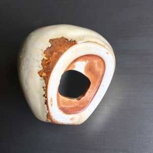 May include: A white ceramic vase with a brown glaze and a hole in the side. The vase has an organic, asymmetrical shape.