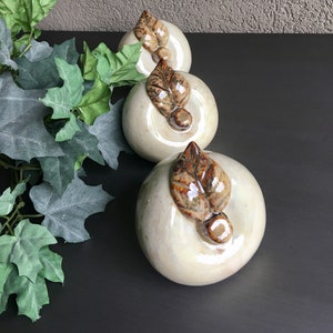 May include: Three ceramic apple figurines with brown leaves. The apples are white with a pearlescent finish.