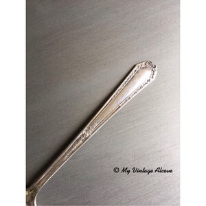 May include: Close-up of the handle of a silver fork with an ornate design. The fork is on a gray surface.