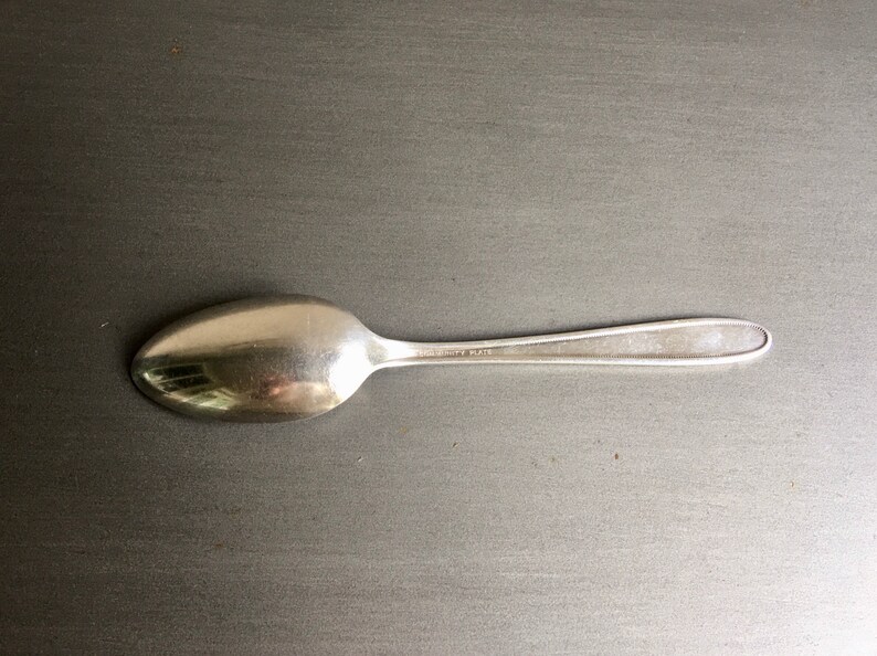 May include: A silver-plated spoon with a rounded bowl and a long, slender handle.