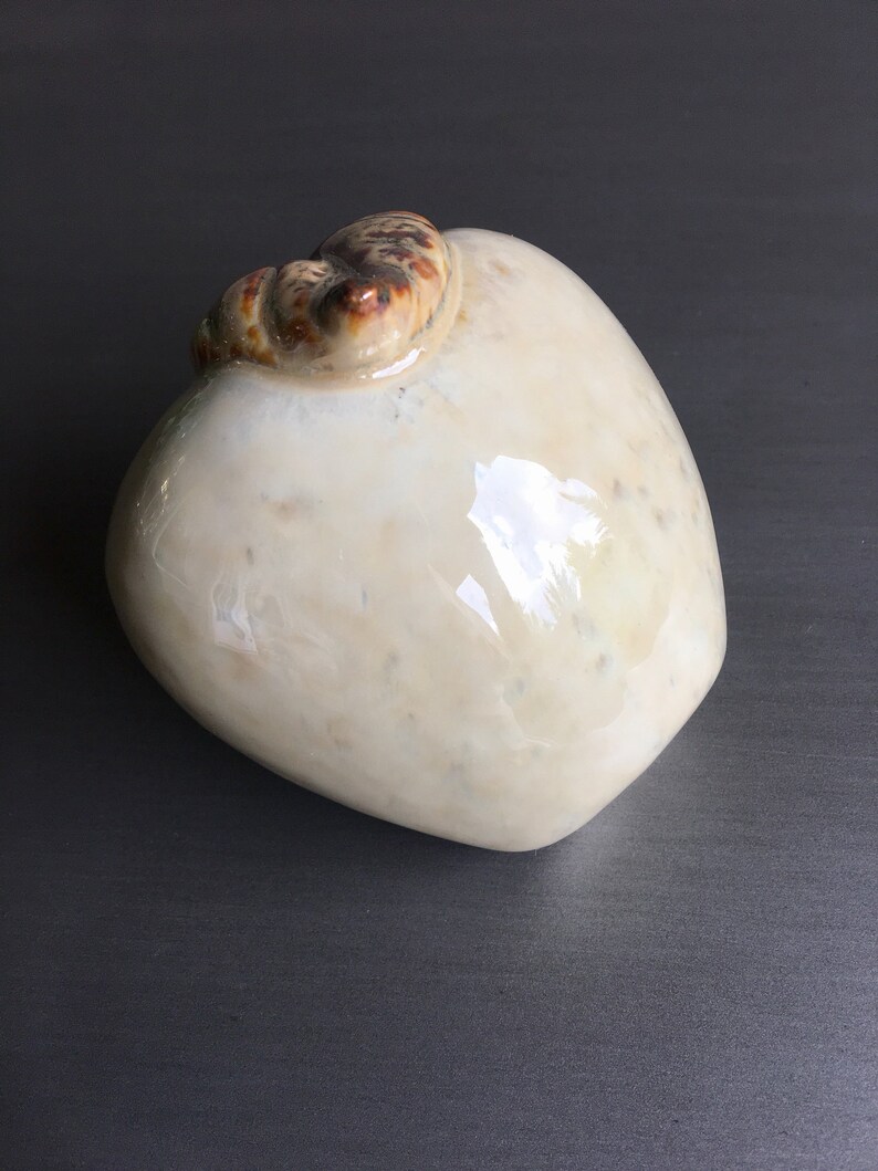 May include: A white ceramic vase with a brown and white swirl design on the top. The vase is shaped like a pear.