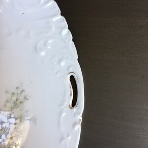 May include: White porcelain serving dish with a floral design and gold trim. The dish has two handles on the sides.