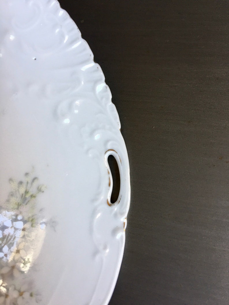May include: White porcelain serving dish with a floral design and gold trim. The dish has two handles on the sides.