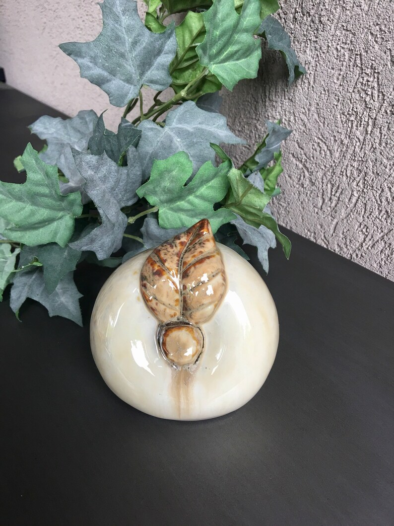 May include: A white ceramic apple with a brown leaf on top. The apple has a glossy finish and is a decorative object.