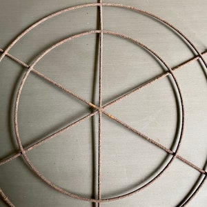 May include: A rusty metal circular frame with a woven wire design. The frame is made of thin wire and has a circular shape with a center point.