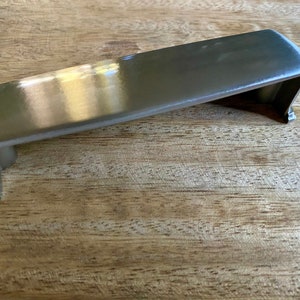 Puede incluir: Un tirador de armario de níquel cepillado con forma rectangular y bordes redondeados.