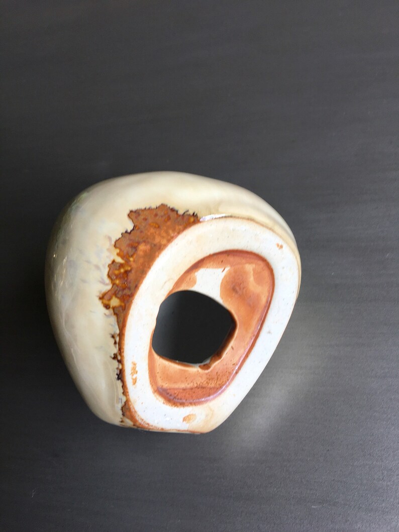 May include: A white ceramic vase with a brown glaze and a hole in the side. The vase has an organic, asymmetrical shape.