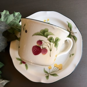 Puede incluir: Un juego de taza y platillo blanco con borde verde y un diseño floral con fresas y hojas.