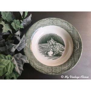 May include: A green and white ceramic soup bowl with a decorative design of a lantern and other objects. The bowl has a scalloped edge and a textured surface.
