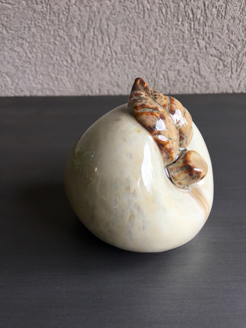 May include: A white ceramic peach figurine with a brown leaf detail. The peach has a glossy finish and a slightly textured surface.