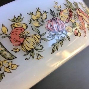 May include: White ceramic bowl with a green, yellow, and pink floral design featuring vegetables like onions, peas, and peppers.