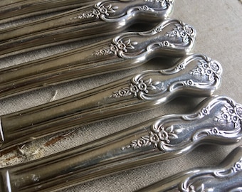 May include: A set of silver-plated dinner knives with ornate floral designs on the handles.