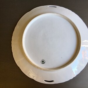 May include: White porcelain serving platter with a scalloped edge and two handles. The platter has a floral design and a small, circular mark on the bottom.