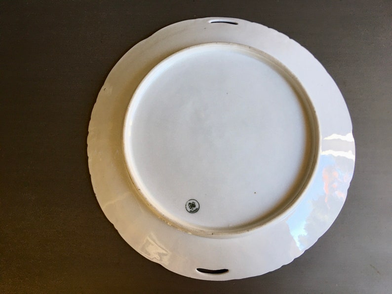 May include: White porcelain serving platter with a scalloped edge and two handles. The platter has a floral design and a small, circular mark on the bottom.