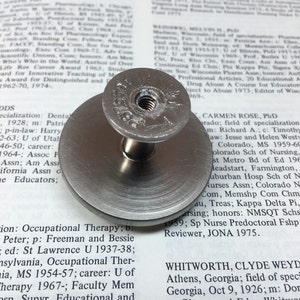 Op de afbeelding: Een zilveren metalen knop met een ronde basis en een schroef met schroefdraad. De knop heeft de gravure "Georgian" erop.