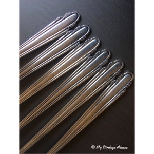 May include: A set of seven silver forks with ornate handles. The forks are arranged in a fan shape, with the handles pointing towards the top of the image. The forks are all in good condition and have a polished finish.