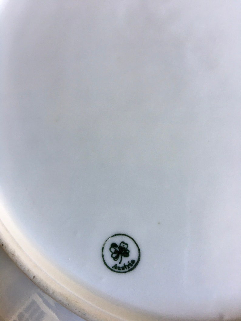 May include: A white ceramic plate with a green shamrock and the word "Austria" in a circle.