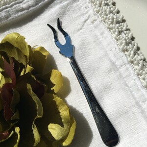 Könnte beinhalten: Eine silberne Gabel mit einem einzigartigen, spitzen Design. Die Gabel liegt auf einem weißen Tuch mit einer Perlenborte.