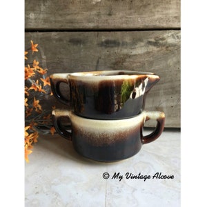 May include: Two brown and white ceramic soup bowls with handles. The bowls are stacked on top of each other. The bowls have a brown glaze with a white rim and a brown and white speckled design.