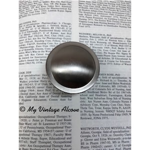 May include: A silver-toned, round, metal door knob with a smooth, polished surface. The knob is surrounded by a white background with black text.