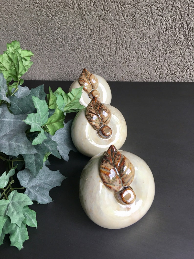 May include: Three ceramic apple figurines with brown leaves. The apples are white with a pearlescent finish.