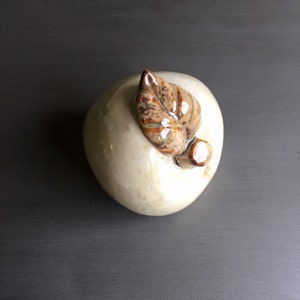 May include: A white ceramic apple with a brown leaf on top. The apple is smooth and has a glossy finish.