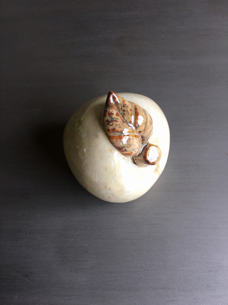 May include: A white ceramic apple with a brown leaf on top. The apple is smooth and has a glossy finish.