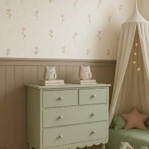 May include: A sage green wooden dresser with four drawers and a scalloped base, topped with two small owl figurines on books. Beside it stands a beige fabric canopy, a star-shaped pillow, and a light green wooden rocking horse on a striped rug.
