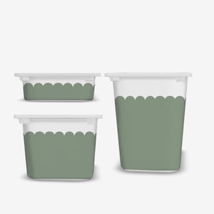 Peut inclure: Trois contenants de rangement blancs et vert sauge avec des bords festonnés. Les contenants sont rectangulaires et cylindriques, avec des couvercles. Le vert sauge couvre la partie inférieure des contenants.