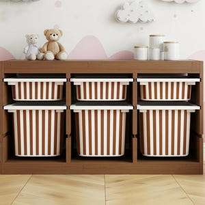 Peut inclure: Unité de rangement en bois avec six bacs à rayures marron et blanc. Deux ours en peluche et un petit animal en peluche sont posés sur le dessus, ainsi que plusieurs boîtes blanches. Un cheval à bascule blanc est à droite.
