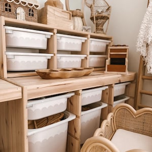 Op de afbeelding: Houten opbergunit met meerdere vakken, elk met een witte bak met een geschulpte rand. Een houten serveerschaal en een rotan poppenbedje zijn ook zichtbaar.