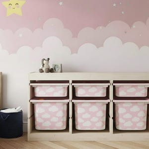 May include: A light wood storage unit with six pink and white cloud-patterned bins. The bins are arranged in two rows of three. The unit is in a child's bedroom with a pink and white cloud mural.