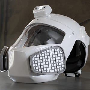 May include: A white helmet with a clear visor and a light on top. The helmet has a gray filter on the front and black accents. The design is futuristic and industrial.
